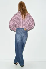 Jeans de tiro alto con diseño barrel, caracterizado por una silueta curvada y holgada en la zona de los muslos y rodillas, estrechándose hacia el tobillo. Cuenta con cinco bolsillos y cierre frontal con cremallera y botón.