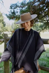 Ruana de tejido de punto en color negro con diseño de rayas verticales blancas y terminaciones con flecos en los bordes.