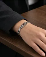 Pulsera esclava de acero con eslabones decorados con esmalte negro y un eslabón central alargado que contiene tres circonias móviles.