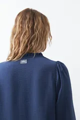 Camisa negra de corte clásico con escote en V, botones frontales y mangas largas con puños. Presenta detalles de recortes calados en la zona de los hombros.