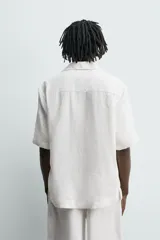 Camisa de lino color blanco, con ajuste relajado, cuello bowling, manga corta y cierre frontal de botonadura.