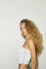 Top bandeau color crema con escote recto, hombros descubiertos y detalle de volantes en capas.