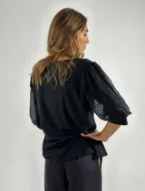 Blusa negra de manga 3/4 con cuerpo de algodón liso y mangas abullonadas de tejido transparente y arrugado.