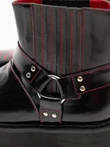 Bota corta de cuero negro tipo biker, con suela track de goma, plataforma, costuras y bordados decorativos en hilo rojo. Presenta tiras con hebillas metálicas y cierre en la parte trasera.