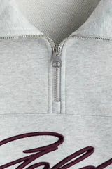 Buzo gris melange de tejido pesado de algodón con hombros caídos y cuello elevado con medio cierre. Presenta puños y bajo en punto acanalado, con el texto 'Golden' bordado en color bordó en el pecho.