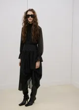 Vestido midi de gasa negro con estampado de lunares blancos, cuello alto, manga larga con volados en los puños y falda con vuelo.