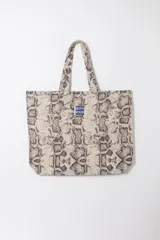 Tote bag de tela con estampado animal print de serpiente en tonos beige y marrón, con doble asa de hombro y parche central con la inscripción "Bonjour".