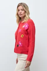 Cardigan de punto color rojo con cierre frontal de botones y bordados de flores en diversos colores. Presenta cuello redondo y mangas largas con puños acanalados.