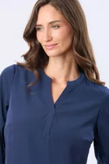Blusa de manga larga en color azul marino, con escote en V y diseño de doble capa en el frente. Presenta puños elásticos y un pequeño aplique metálico decorativo en el ruedo.