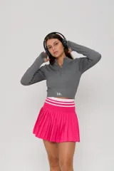 Top deportivo de manga larga en color gris, confeccionado en tejido acanalado. Presenta un diseño ajustado al cuerpo, cuello alto con cierre frontal parcial y aberturas para los pulgares en los puños. Incluye el logo 'bk.' estampado en la parte inferior frontal.