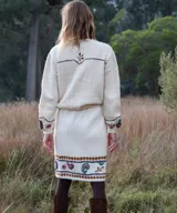 Cardigan tejido de punto color marfil, con bordados artesanales florales y paisley, cierre frontal de botones y detalles de costuras a contratono.
