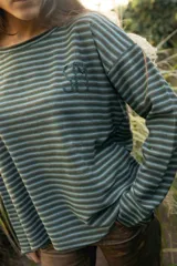 Remerón de manga larga con diseño de rayas horizontales finas en tonos tierra. Presenta un corte holgado y cuenta con un bordado artesanal en color rojo en el pecho.