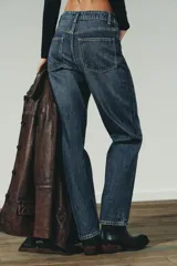 Jeans de mujer, tiro alto, color azul medio con efecto desgastado (lavado claro en muslos y oscuro en bordes). Corte recto y ancho (mom fit) con cinco bolsillos y cierre frontal de botón y cremallera.