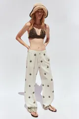 Pantalón color crema de tiro medio con cintura elástica ajustable y bolsillos delanteros. Presenta bordados florales en negro y corte ancho.