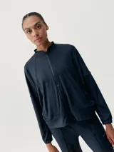 Chaqueta deportiva color azul marino, con cierre frontal, cuello alto y mangas murciélago. Presenta un calce holgado y bolsillos laterales.