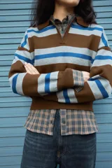 Jersey de punto con diseño a rayas horizontales en tonos marrón, gris y azul. Presenta cuello tipo polo con abertura frontal, manga larga y puños acanalados.