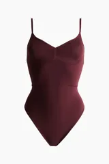 Body tanga modelador color borravino con efecto vientre plano y copas sin aros que realzan el busto. Cuenta con breteles finos ajustables y diseño sin costuras laterales.