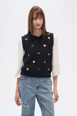 Chaleco de punto color azul marino, con cuello V y diseño de rombos trenzados. Presenta múltiples apliques bordados de motivos variados como mariposas, cerezas, flores, soles, lazos, limones, fresas, sonrisas, rosas y trozos de pizza.