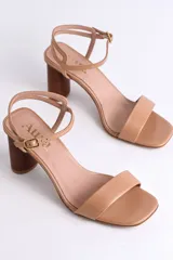 Sandalia de cuero color peltre, con tira ancha sobre los dedos y tira fina con hebilla al tobillo. El taco es cilíndrico de madera clara.