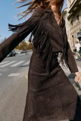 Chaqueta corta de Zara confeccionada en tejido efecto ante color marrón oscuro. Presenta cuello con solapas de muesca, manga larga y detalle de flecos en el mismo tejido a lo largo del pecho y la espalda. Cierre frontal cruzado con botones ocultos.