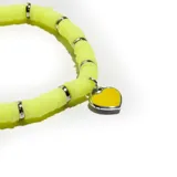Pulsera elástica con cuentas de goma amarillas y separadores metálicos plateados. Incluye un dije colgante en forma de corazón amarillo con borde plateado.