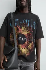 Camiseta de punto negro con efecto lavado, corte relaxed fit y cuello redondo. Presenta un estampado frontal con tipografía gótica en azul y una imagen circular que simula un iris en tonos rojizos y amarillos.