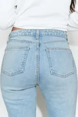 Jeans de tiro alto con diseño cropped flare, confeccionados en denim azul con acabado desgastado. Presentan cinco bolsillos, cierre frontal con cremallera y botón metálico, y bajo con terminación sin costuras.