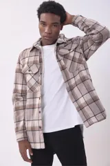 Sobrecamisa de corte holgado con diseño a cuadros en tonos beige y marrón, confeccionada en tejido de textura suave. Presenta cuello clásico, cierre frontal con botones, dos bolsillos con solapa en el pecho y puños abotonados.