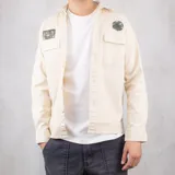 Sobrecamisa color arena de gabardina con cuello camisero, cierre frontal con botones, dos bolsillos de parche con solapa abotonada en el pecho y parches decorativos bordados.