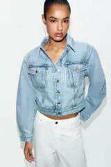 Cazadora corta de denim color celeste con cuello solapa, manga larga y hombreras. Cuenta con bolsillos delanteros con solapa y cierre frontal de botones metálicos.