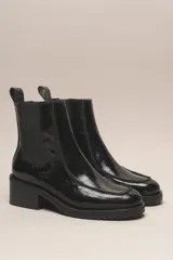 Bota Chelsea de cuero charol negro, con elástico lateral, punta cuadrada y taco bajo.