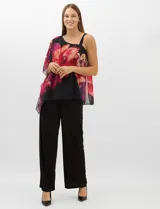 Enterito de seda fría con pantalón corte palazzo de pierna ancha. Presenta un diseño de un hombro descubierto con tirante fino y una sobrecapa asimétrica de gasa estampada con motivos florales en tonos rojos y fucsia sobre fondo negro que cae desde el hombro derecho.