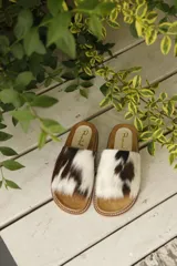 Sandalias bajas con base color suela y capellada de piel de vaca con manchas marrones y blancas.