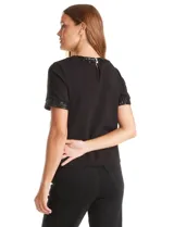 Blusa negra de manga corta con cuello redondo y puños decorados con ribetes de lentejuelas brillantes. Confeccionada en tejido suave y fluido, presenta una silueta recta y cierre de ojal con botón en la espalda.