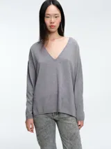 Sweater de punto gris con escote en V profundo, hombros caídos y mangas largas. Presenta un diseño de calce relajado con sutiles micro lentejuelas integradas en el tejido.