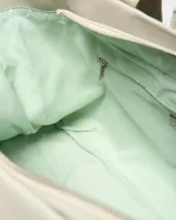 Cartera tipo tote color beige con asas de hombro decoradas con el texto impreso de la marca, bolsillo frontal y parche circular grabado con el logotipo en la parte inferior.