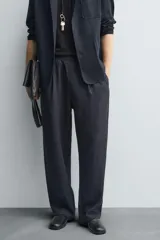 Pantalón negro de corte relajado con cintura elástica ajustable y pliegues en la parte delantera. Presenta bolsillos laterales y bolsillos traseros de parche.