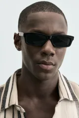 Camisa de manga corta con calce relaxed fit, confeccionada en tejido estructurado con algodón. Presenta un diseño de rayas verticales en tonos beige, negro y blanco, cuello solapa, cierre frontal con botones y aberturas laterales en el bajo.