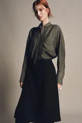 Blusa color gris con finas rayas verticales negras, cuello redondo con lazo del mismo tejido, manga larga con puño, bolsillos de parche en el pecho, bajo asimétrico y cierre frontal oculto con botones.