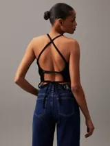 Top negro de denim rígido con cuello halter, diseño entallado y cropped, costuras moldeadoras en el pecho, espalda abierta con cierre anudado y logo de Calvin Klein en el bajo.