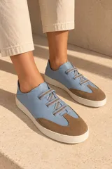 Championes de cuero vacuno color celeste con puntera de gamuza marrón, suela de goma y cordones elásticos.