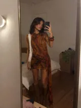 Vestido corto de cuello halter con estampado abstracto en tonos marrones y naranjas. Presenta un diseño ajustado con un detalle de nudo lateral y una caída de tela asimétrica con bordes ondulados.