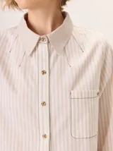 Camisa de algodón con estampado de rayas verticales en tonos beige y blanco. Presenta cuello clásico, cierre frontal con botones tipo carey y un bolsillo frontal con costuras en contraste.
