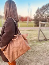 Bolso grande tipo tote de cuero color marrón gastado, con doble asa corta de madera y correa larga de tela estampada.
