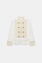 Chaqueta de estilo militar de ZARA Woman Collection, confeccionada en mezcla de algodón en color blanco y beige. Presenta cuello subido, manga larga con puños anchos en contraste y cierre frontal con alamares y botones metálicos en relieve. Tiene bajo asimétrico con abertura en la espalda.