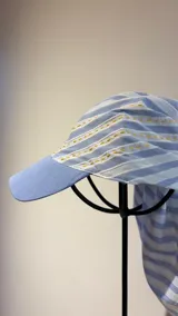 Gorro tipo visera con pañuelo integrado de algodón a rayas celestes y blancas, con detalles de bordado manual en hilo amarillo.
