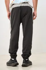 Pantalón de jogging gris oscuro con banda lateral gris claro, cintura elástica con cordón ajustable, bolsillos laterales con cierre y puños elásticos.