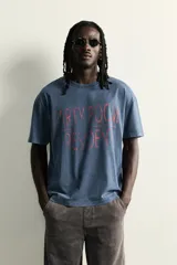 Remera de corte relaxed fit con efecto lavado, cuello redondo y manga corta. Presenta un estampado frontal de texto en tono contrastante.