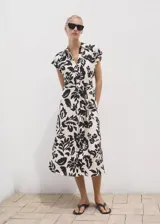 Vestido midi de corte recto con estampado floral en contraste. Presenta cuello camisero, cierre frontal de botones, mangas cortas y cinturón ajustable en la cintura del mismo tejido.