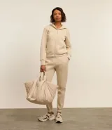 Pantalón deportivo femenino color beige, confeccionado en mezcla de algodón y poliéster, con cintura elástica y frisos delanteros verticales.